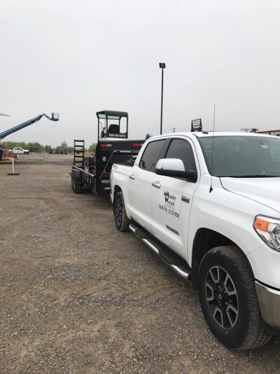 Branded Monkey Wrench Plumbing truck towing a trailer with equipment at a job site